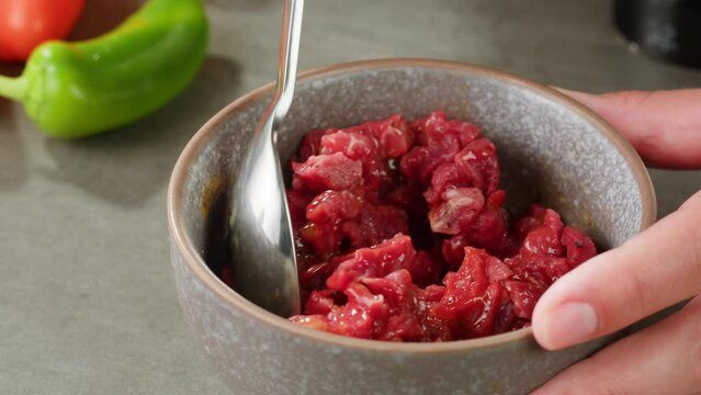 Chef cooking Raw beef meat tartar with sauce, man cutting steak tartare, making delicious french dish in modern restaurant. Fresh eco angus meat. 