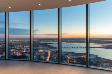 Fotobehang View from a high-rise building overlooking a city at sunset. The view is from a room with floor-to-ceiling windows that are framed in black, and the floor is made of light-colored wood © Florian