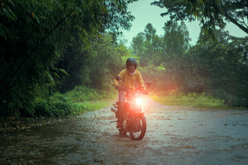 man riding small endurom motorcycle crossing shallow creek among rain falling at forest - obrazy, fototapety, plakaty