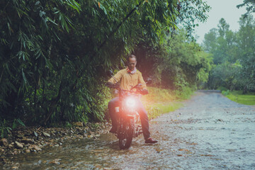 asian man riding small enduro motorcycle crossing flowing creek in forest among rain falling