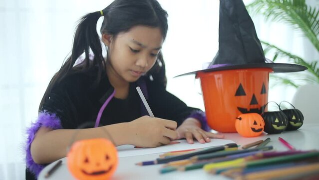 Asian little girl with coloring pencils drawing witch on paper at home.Halloween concept.