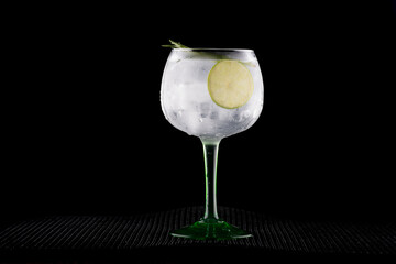 glass of gin and tonic drink with lemon and rosemary on dark background in front rubber holder