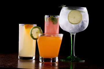 mix of colorful cocktails in front of a table in close-up with a glass of gin and tonic