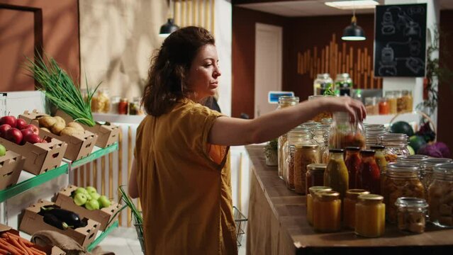 Woman purchasing pantry staples from zero waste supermarket, proceeding to pay for them at checkout counter. Customer in local grocery store shopping for bulk items in reusable metal jars