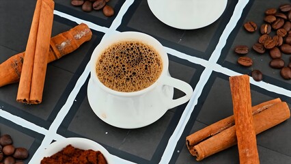 Cup of coffee, cinnamon sticks and star anise on saucer. Grains of coffee and cinnamon on table. White background. Top view