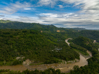 Green mountain with river with muddy water. Blue sky and clouds. Mindanao, Philippines.