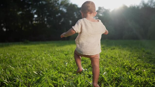 baby takes first steps in the park. happy family kid dream concept. son baby to walk takes the first steps in the park on green grass. baby son taking first steps lifestyle