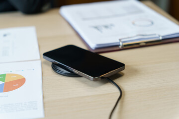 Charging mobile phone battery with wireless charging device in the table. Smartphone charging on a charging pad. Mobile phone near wireless charger Modern lifestyle technology concept - obrazy, fototapety, plakaty