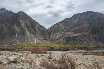 Scenic view of Himalayas and Ladakh ranges. Beautiful barren hills in Ladakh with dramatic clouds in the background.  Road side view, Shyok river , rocks and greenery in base of the mountains.