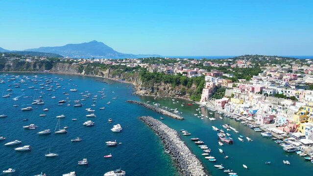 Impressive aerial pullback from Panoramica sulla Corricella on Procida Island (Isola di Procida) of the blue Tyrrhenian Sea in the Gulf of Naples with pastel buildings, white boats and mighty Vesuvius