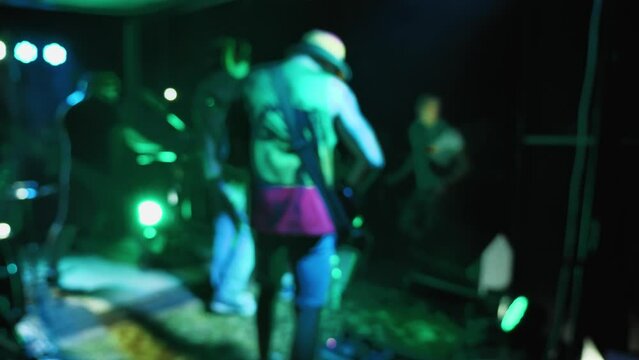 Reggae band performing on an outdoor stage. People are dancing in front of the musicians. Side view of musicians playing on stage in the light of multicoloured spotlights. Slow motion. Blurred video