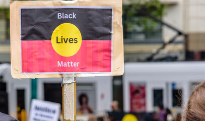 A homemade protest sign with a 'Black Lives Matter' political message on the aboriginal flag is held up by a wooden post - obrazy, fototapety, plakaty