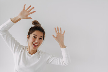 Happy Thai Asian woman bun hair, waving both hands gesture to say hello look above empty space,...
