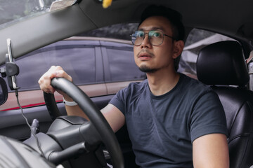 Asian Thai man with beard,  wear eyeglasses parking a car, looking at rear view mirror while...