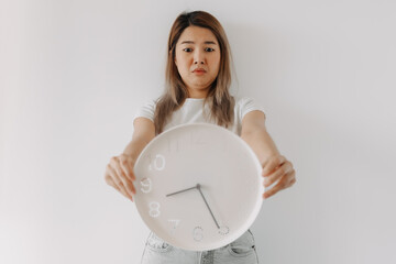 Asian Thai woman holding and looking at white clock showing time with funny unexpected anxious face. Having no enough time, busy in the morning rush hour, go work late.