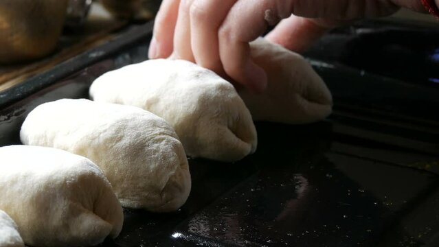 Female hand puts in a row homemade cakes raw dough on a special metal baking sheet in a rustic style. The dough in the form lies ready for the oven