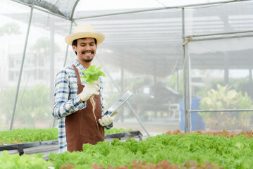 Farmer cheerful young gardener in overall standing with seedlings in greenhouse. Portrait of joyful farmer.