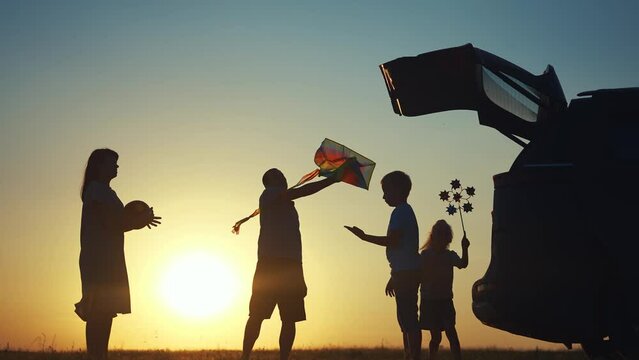 family traveling by car. family watching the sunset silhouette next to the car in the park. family playing kite ball. people in the park lifestyle. family car camping resting in nature