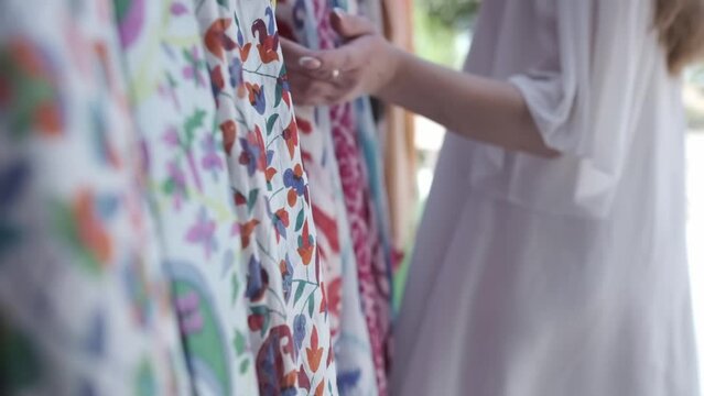 A young woman with long hair in a light sundress chooses bright oriental fabrics
