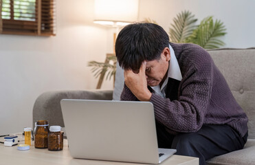 An elderly man with a headache is studying information about a medicine before taking it. Stressed elderly man Find drug information on your laptop