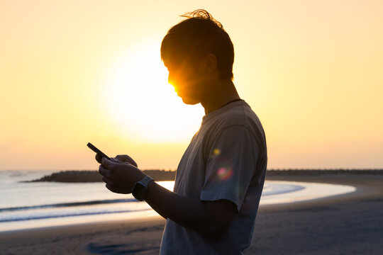 Silhouette of man use mobile phone at sunset in the beach
