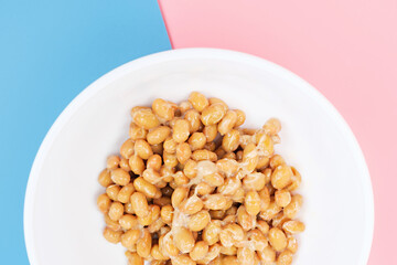 Japanese natto beans in a white bowl close-up on pink and blue background.