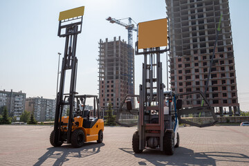 Two forklift trucks near skyscrapers under construction