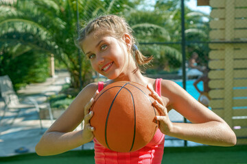 A cheerful attractive teenage girl is holding a basketball in her hands
