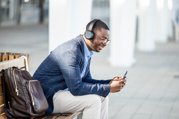 Handsome man in elegant suit listening to music and using smart phone in the city.
