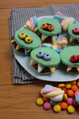Multicolored toothed monster cookies with chocolate cream on a plate with candies. Halloween sweet food