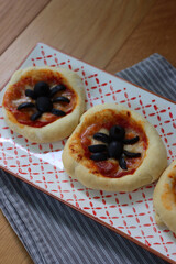 Halloween mini spider pizzas with black olives on a ceramic tray on wooden table