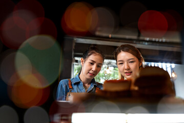 Asian woman waitress holds a digital tablet and help customer choose or select cake in display case. Small business, Business owner.