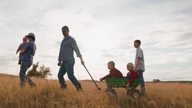 Mother carries baby father pulls brothers in cart walking with family in field