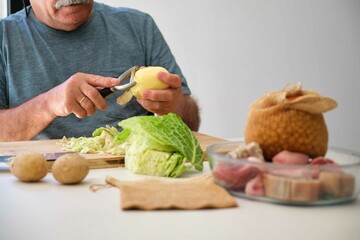 Mature Spanish man peeling potatoes to prepare cocido madrileño, typical Spanish dish.
