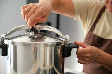 Mature Spanish woman placing regulator whistle on pressure cooker to prepare cocido madrileño.