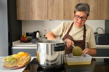 Mature Spanish woman straining off the stock of the cocido madrileño, typical Spanish dish.