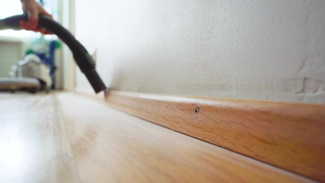 Man cleaning off the dust on a baseboard with a vacuum cleaner