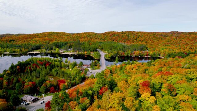 Scenic Fall road trip top down aerial view through rolling hills small town colorful trees and bridge across a lake
