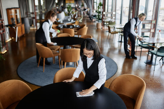 High Angle View At Servers Wiping Tables In Classic Uniform Preparing Luxury Restaurant For Grand Opening, Copy Space