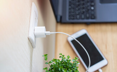 White plug in power outlet adapter cord charger of mobile phone on wooden floor.