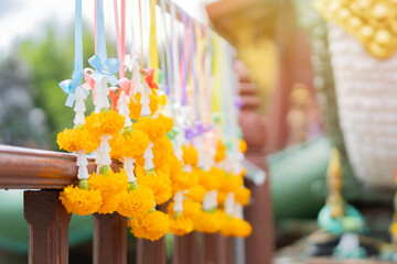 Thai artificial yellow marigold garland hang at the hanger and background in Thailand ancient temple.