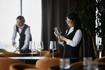 Side view portrait of young Asian woman polishing wine glass in luxury restaurant setting, copy...
