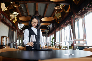 Portrait of elegant Asian woman as female server setting tables in luxury restaurant preparing for guests, copy space