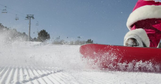 Santa Claus on snowboard on snowy slope. Professional male snowboarder in Santa Claus costume rolls down snow slope. Unforgettable New Year's Christmas atmosphere full of laughter and fun. slow motion