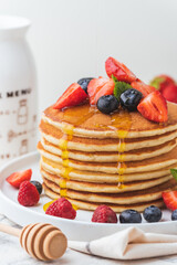 Stack of fresh pancakes with strawberries and blueberries drizzled with maple syrup and honey. Healthy traditional American breakfast on the white background