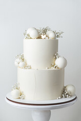 Big bunk wedding cake covered with white chocolate frosting and decorated with white chocolate spheres on the white background.