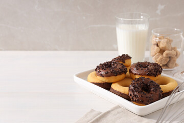 Chocolate donuts on plate, glass of milk and jar of sugar on light background, space for text