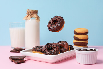 Chocolate donuts on plate, chocolate and bottle of milk on blue background