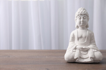 White statue of Buddha on wooden table on light background, space for text