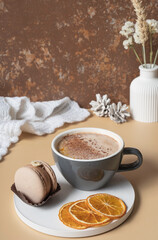 A cup of warm cocoa with a macaroon and cozy winter decor. Winter still life with a warm drink